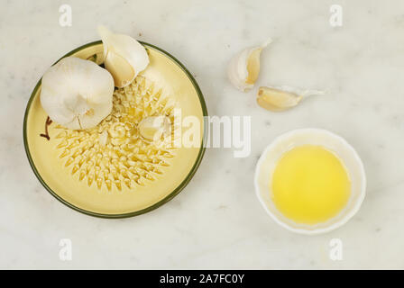 Aglio in una grattugia piastra con olio di oliva su un piano di lavoro in marmo, vista dall'alto Foto Stock