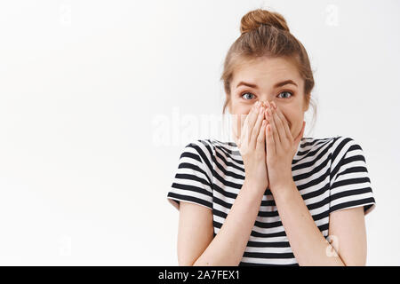 Close-up sorpreso, stupito senza parole bella donna in striped t-shirt con bun disordinato, coprire la bocca come la reazione di stupidi e stupiti di awesome Foto Stock