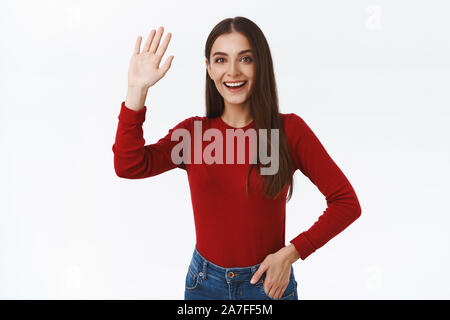 Cordiale, entusiasta bella bruna studentessa in maglione rosso, alzando la mano fino in alta cinque o sventolare nel saluto, dire ciao ciao o con Foto Stock