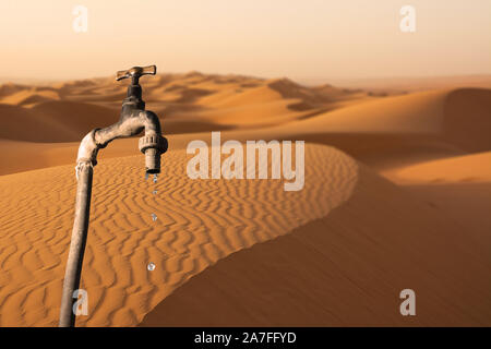 Rubinetto che gocciola e ambiente desertico in background, concetto di riscaldamento globale del pianeta e per la scarsità di acqua Foto Stock