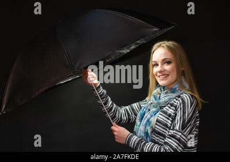 Giovane femmina modello dalla Polonia in posa di studio. Ragazza con sorriso carino, cortese espressione faccia tenuta Ombrello nero. Foto Stock