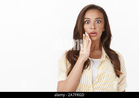 Vita-up impressionato senza parole senza fiato bruna giovane donna in camicetta su t-shirt, aprire la bocca e lo sguardo attonito, tenere la mano vicino a labbri hanno teso una imboscata Foto Stock