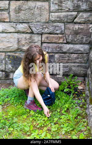 Giovane donna felice ragazza raccolta foraggio verde selvatico tarassaco lascia per la salute nel parco da parete in legno di piegatura ad angolo su accovacciato Foto Stock