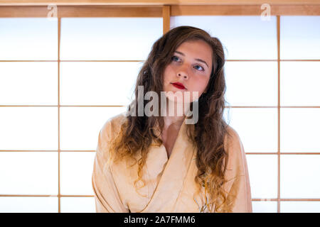 Casa tradizionale giapponese con il vetro della porta scorrevole con caucasian donna in costume di kimono in piedi che guarda in alto Foto Stock