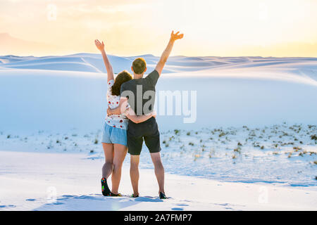 Uomo e donna coppia giovane permanente sulla collina di sabbia in White Sands Dunes National Monument in New Mexico con tramonto Foto Stock