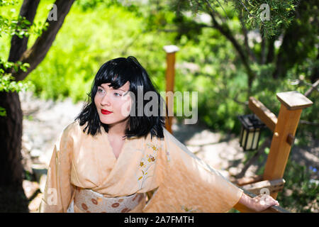 Giovane donna in kimono costume fino a piedi con ringhiera in legno recinto nel giardino esterno in Giappone con la natura vista Foto Stock