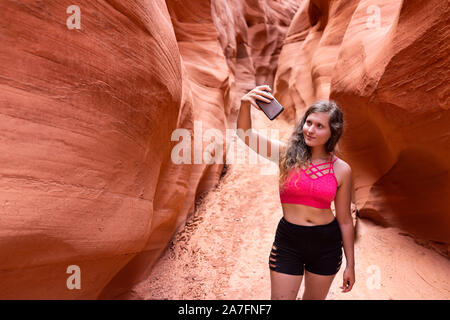 Giovane donna ragazza tenendo selfie foto con il telefono sulla passeggiata da forme d'onda a slot Antelope Canyon in Arizona durante l'estate sport con pantaloncini corti e bra Foto Stock