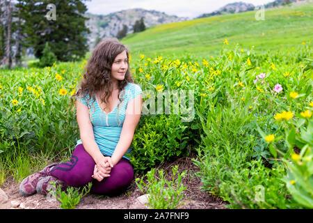 Albion bacino, Utah donna seduta da fiori gialli in estate prati trail nel 2019 in montagne Wasatch durante il festival di fiori selvaggi stagione Foto Stock