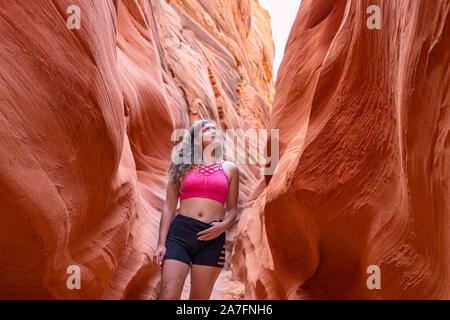 Giovane donna in piedi che guarda sulla passeggiata da forme d'onda in corrispondenza stretta fessura Antelope Canyon in Arizona durante l'estate sport con pantaloncini corti e bra Foto Stock