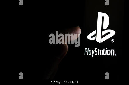Il logo PlayStation su una schermata dello smartphone in una stanza buia e un dito di toccarlo. Foto Stock