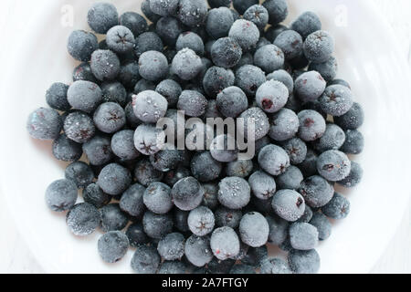 Piastra bianca con congelati bacche chokeberry su una tavola di legno tavolo bianco. Close-up. Foto Stock