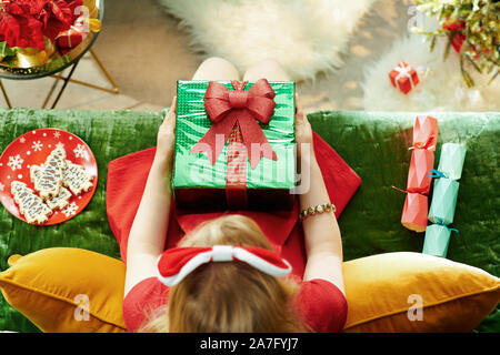 Stagione di vacanze. Vista superiore della elegante piccola principessa in abito rosso seduto sul divano nel soggiorno moderno a Natale Natale tenendo presente b Foto Stock