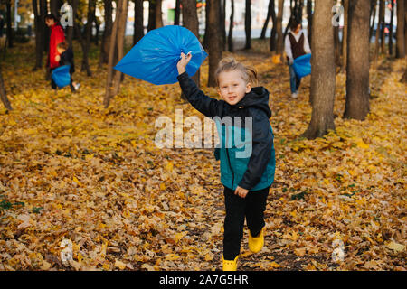 Little Boy saltare a piedi con un sacchetto di rifiuti in una foresta stagionale in autunno Foto Stock