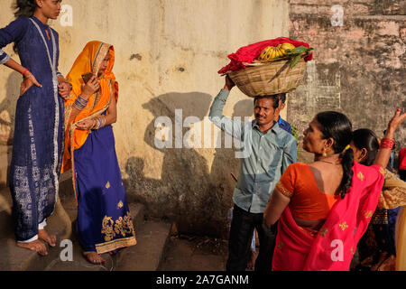 Una famiglia indù al serbatoio Banganga, Walkeshwar, Mumbai, India, durante la celebrazione della festa Chhath Puja, il padre che trasportano le offerte sacrificali Foto Stock