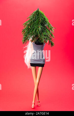 La bambola dal vivo con un albero di Natale in mano, vestito di un nero ed un abito bianco su sfondo rosso, composizione di Natale Foto Stock