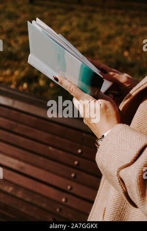 La donna in un autunno ricoprire tiene un libro. Autunno park in una giornata di sole Foto Stock