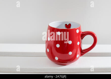 Un rosso mug di pois sorge su un ripiano bianco in una giornata di sole. Foto Stock