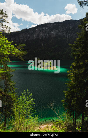 Piccola isola sul Eibsee bavarese lago ai piedi della coperta di neve Zugspitze con chiare acque azzurre, il bianco delle nuvole e cielo blu durante l'estate (Grainau) Foto Stock