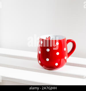 Un rosso mug di pois sorge su un ripiano bianco in una giornata di sole. Foto Stock