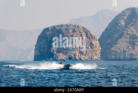 Barca galleggiante sul mare circondata da rocce nel deserto vicino a Khasab Musandam, Oman Foto Stock