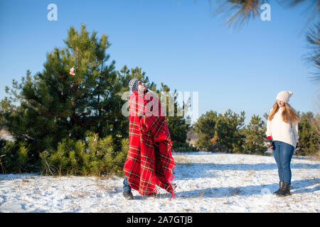 Passeggiata invernale nella foresta. Un ragazzo in un rosso plaid plaid pone come un supereroe, considerando che il plaid è il suo mantello. Il supereroe che meritano. Foto Stock