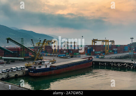 Da Nang, Vietnam - Marzo 10, 2019: Tien Sa Porto di Da Nang Bay. Piccolo fiume nave da carico Huang SA 09, ancorata al cantiere di contenitore con pile di scatole e Foto Stock