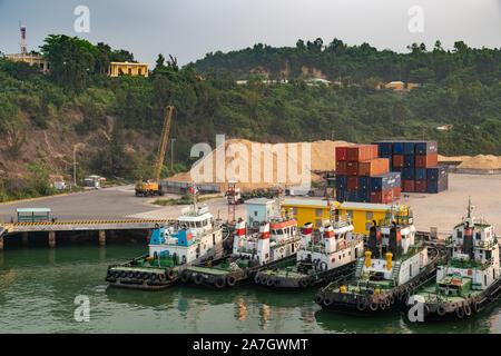 Da Nang, Vietnam - Marzo 10, 2019: Tien Sa Porto di Da Nang Bay. Cinque rimorchiatori ancorato nel dock con il blu e il rosso di scatole di contenimento, un enorme pila di yello Foto Stock