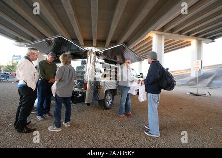 Volontari con Mobile pani e pesci, una Austin-basato programma del ministero la distribuzione di pasti per i senzatetto, out invece pasti in un accampamento di senza tetto sotto un cavalcavia autostradale di Austin. Foto Stock