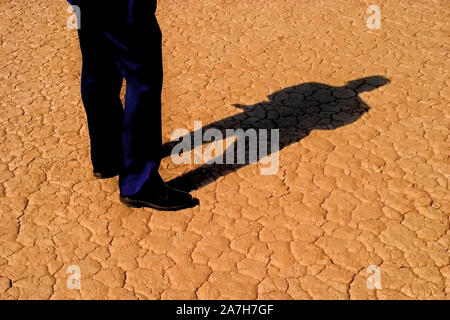 L uomo per le gambe in business giochi e corpo pieno ombra sul deserto incrinato terreno Foto Stock