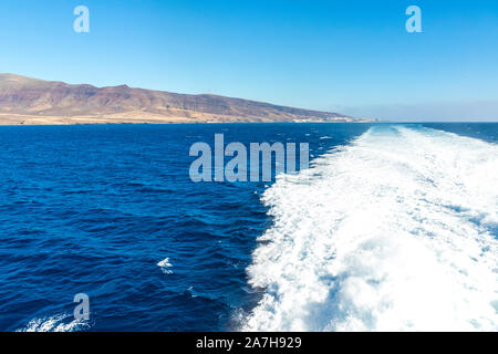 Sentiero dell'acqua la formazione di schiuma dietro un ferry boat in oceano Atlantico tra le isole Canarie, Spagna. Isola di Fuerteventura sullo sfondo Foto Stock