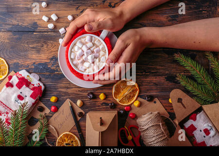 Donna mani tiene una tazza di cacao a caldo con marshmallows stoffa a maglia per una tazza il concetto di natale Foto Stock