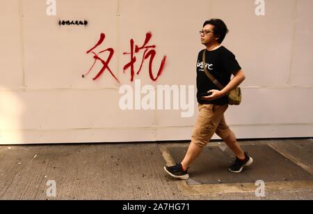 Hong Kong, Cina. 3 Novembre, 2019. Un giovane uomo a piedi passato una facciata in legno al di fuori di Banca di Cina, che viene spruzzata su una delle parole cinesi, resist.Nov-3, 2019 Hong Kong.ZUMA/Liau Chung-ren Credito: Liau Chung-ren/ZUMA filo/Alamy Live News Foto Stock