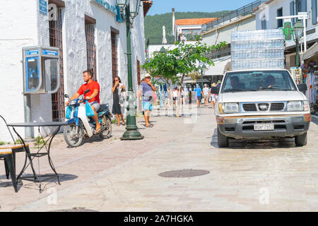 Skiathos Grecia - 4 agosto 2019; il carrello caricato con plastica bottiglie di acqua che viene erogata in strada con i turisti e il motociclista in tipico greco ISL Foto Stock