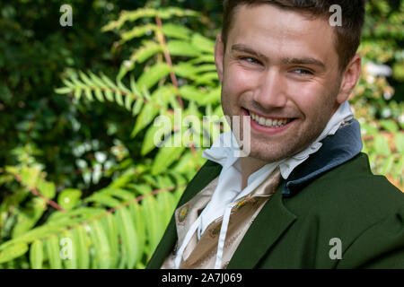 Ritratto di bello uomo sorridente vestito in costume d'epoca seduta sul banco in giardino Foto Stock