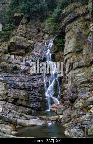 Esposizione a lungo una piccola cascata circondata da pietre durante il giorno in Cina Foto Stock