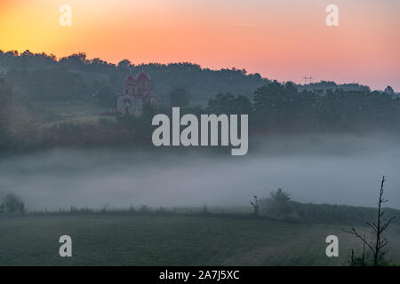 Bellissima la mattina presto landskape da una nebbia strada da qualche parte in Serbia,con qualche santo sacramento in una distanza Foto Stock