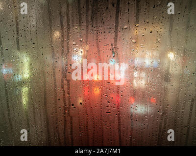 Gocce di pioggia su una finestra di bus con fari sfocata dietro Foto Stock