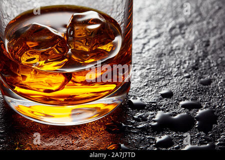 Bicchiere di whiskey elegante con cubetti di ghiaccio sulla pietra nera tabella. Moody vista ravvicinata Foto Stock