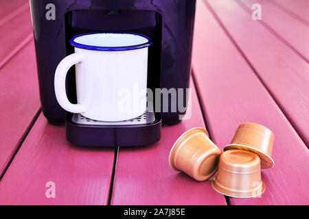 Espresso Cappuccino macchina, capsule e un boccale di vintage su una rosa un tavolo di legno. Capsula di mattina la preparazione del caffè. Foto Stock