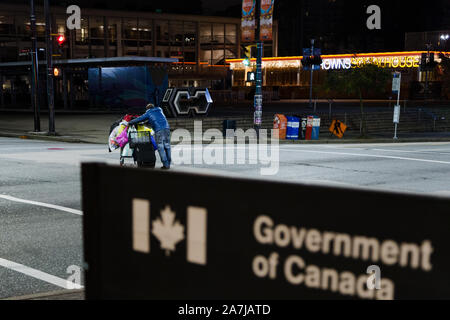 VANCOUVER, BC, Canada - Ott 05, 2019: un uomo senza tetto con un carrello di shopping come oggetto di attenzione passando da un governo del Canada, al di fuori della messa a fuoco Foto Stock