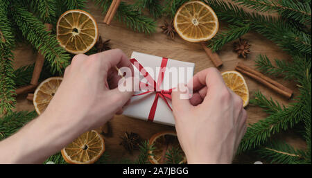 Vista dall'alto man mano la legatura red ribbon bow sulla scatola regalo decorata su tavola in legno di quercia, wide photo Foto Stock