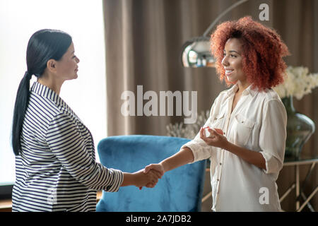 Curly donna sorridente agitando la mano di utili psicanalista Foto Stock