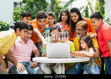 Un gruppo di tre generazioni la famiglia guardando allo schermo del computer portatile e puntare il dito in cortile di casa loro Foto Stock