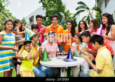 Group-Of grandi famiglie membri in giardino durante la celebrazione di compleanno e Adult-Son il taglio di una torta di compleanno Foto Stock