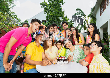 Grande gruppo di famiglia indiano membri tenendo Selfie foto con monopiede durante la festa di compleanno in cortile di casa loro Foto Stock