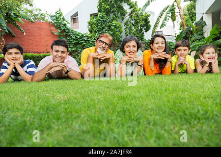 Gruppo di Felice Multi-generazione Famiglia.sdraiato sul-l'erba Relaxting insieme davanti alla loro casa in giardino Foto Stock