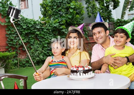 Famiglia Felice e i genitori Two-Children tenendo Selfie foto con lo smartphone su selfie stick durante la festa di compleanno in cortile Of-Their Home Foto Stock