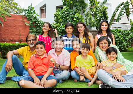 Grande gruppo di famiglia indiana dei soci del soggiorno-su-erba insieme rilassante davanti a casa loro in-il-giardino Foto Stock