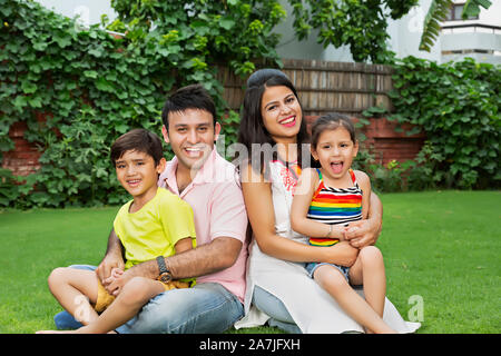 La famiglia felice i genitori e due bambini figlio ed figlia seduta su erba e rilassarsi nel cortile-di-la loro casa Foto Stock