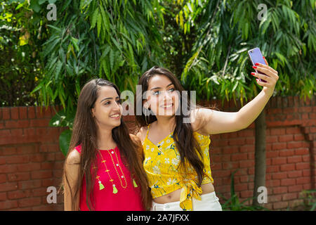 Due giovani donne amici prendendo selfie foto con il cellulare in-giardino esterno Foto Stock